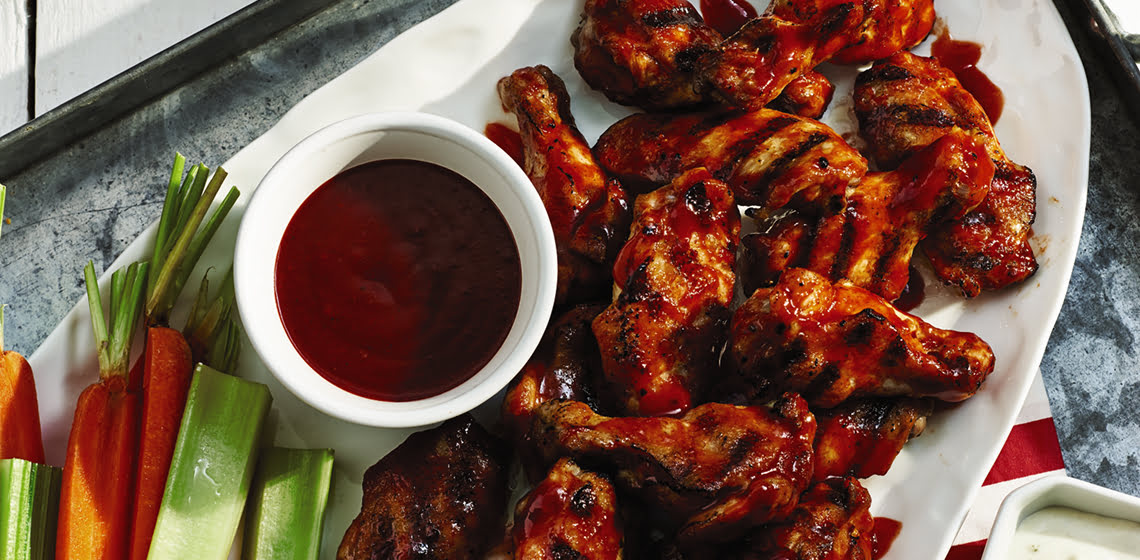 Plate of grilled sriracha chicken wings with a side of sauce and cut celery and carrots.