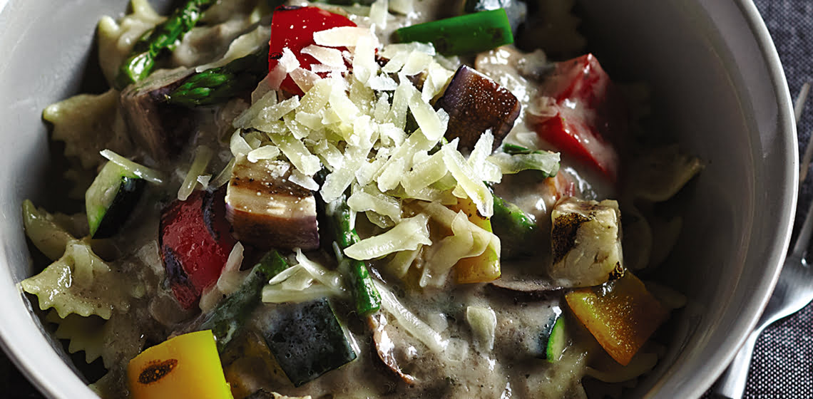 Grilled vegetable and wild mushroom pasta in a grey bowl with a fork and grey napkin on the side