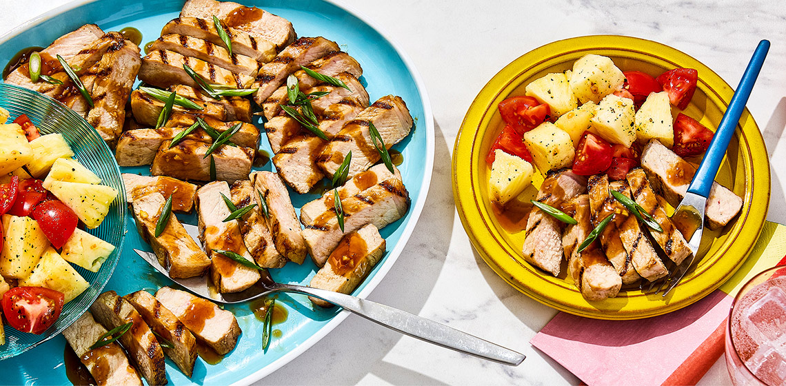 Grilled pork and pineapple salad on yellow plate with serving bowl to the left.