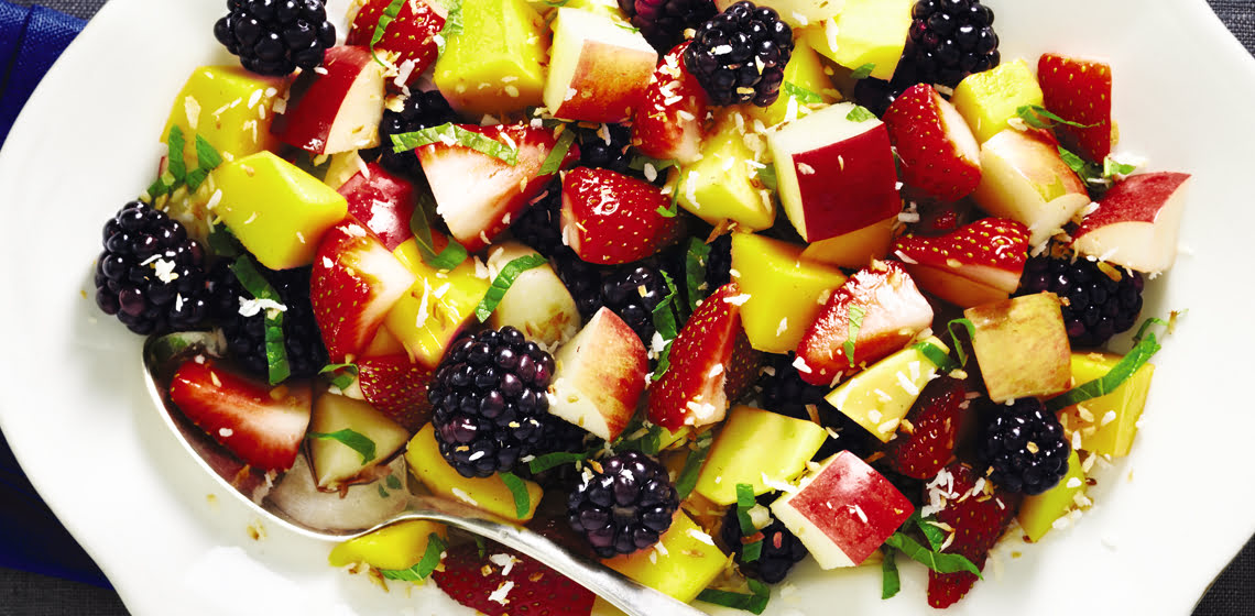 Big white serving plate with a honey and mint fruit salad and a serving spoon.