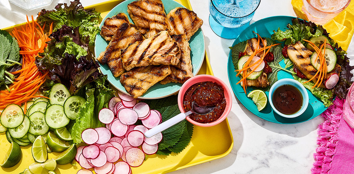 Korean-style pork belly lettuce wrap ingredients on a platter, and two lettuce wraps with a side of sesame dipping oil on a round blue plate.