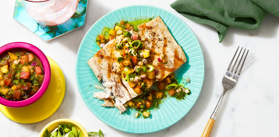 Mahi mahi with the watercress salad on top on a teal plate with a fork beside and a small pink bowl with more salad.