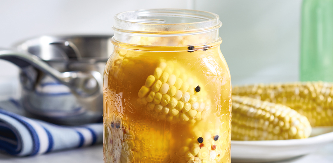  A jar of quick-pickled corn on a white countertop.
