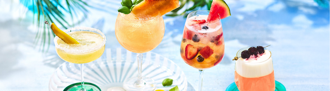 Four cocktails on marble background with green in background.