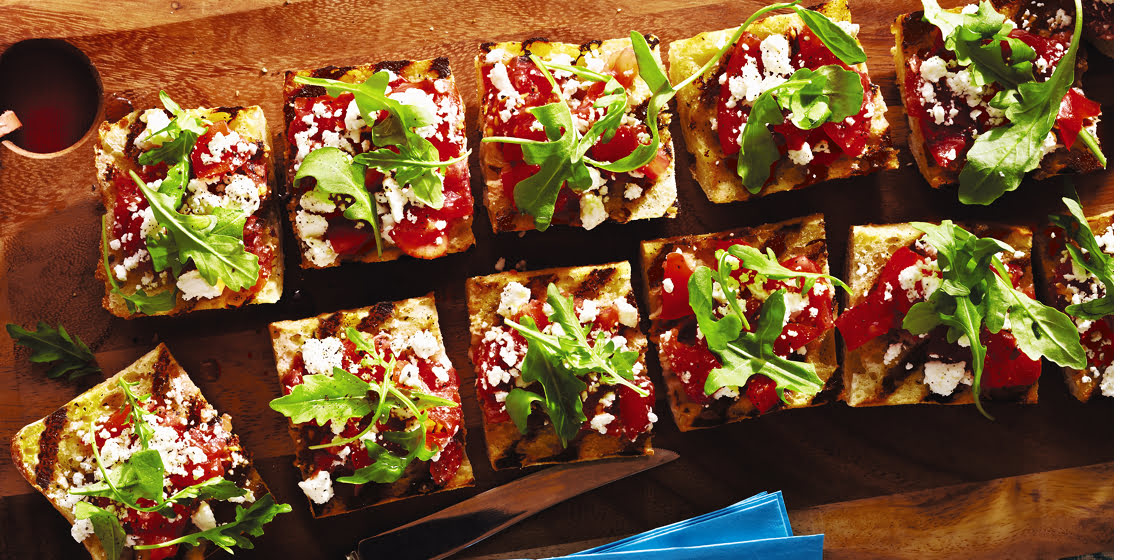 Pieces of bruschetta on a board topped with arugula.