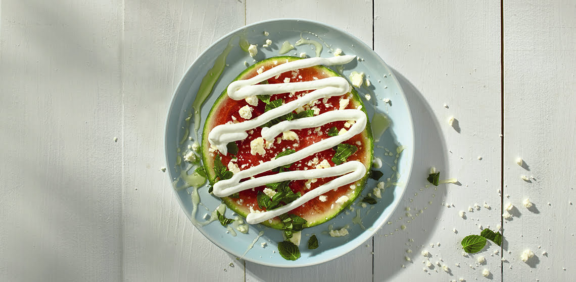 Overhead shot of savoury watermelon pizza on a blue plate.