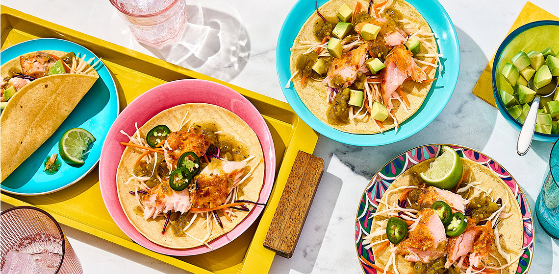 Overhead shot of salmon tacos topped with jalapeno, chili salsa, and slaw. 