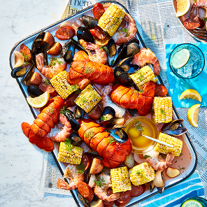Platter filled with seafood boil of lobster tails, corn, mussels, shrimp, potatoes, and lemon.