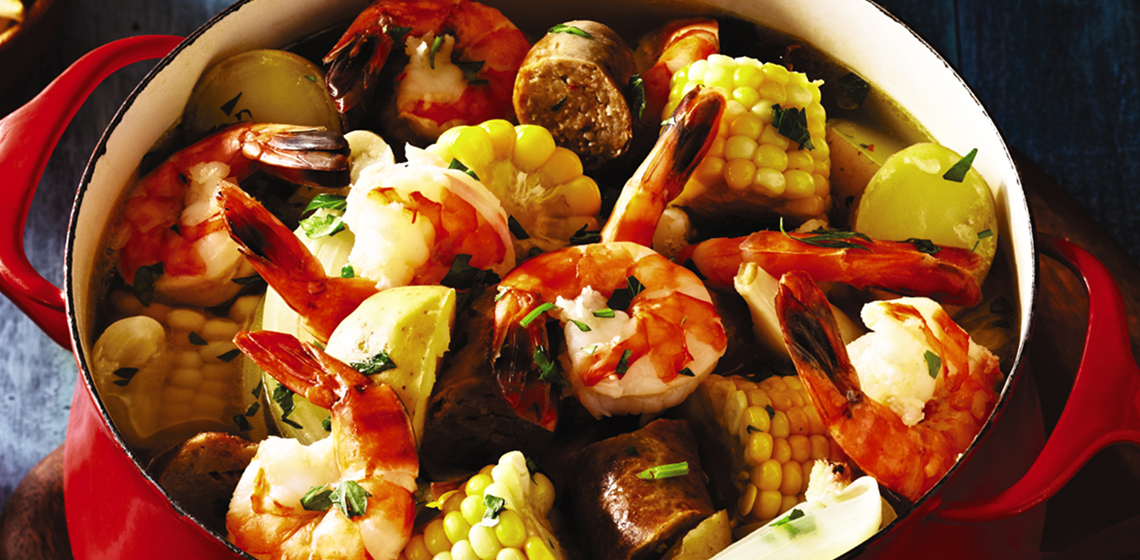 Red pot filled with a shrimp boil on a cutting board with slices of bread