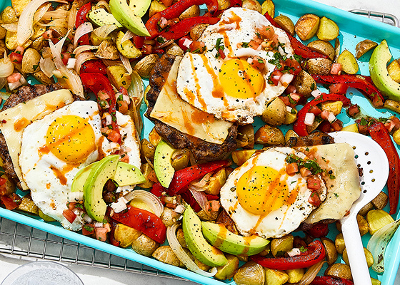 Mexican pan hash on a blue baking sheet with a bowl of tomato salsa and a plate of sliced avocado on the side.