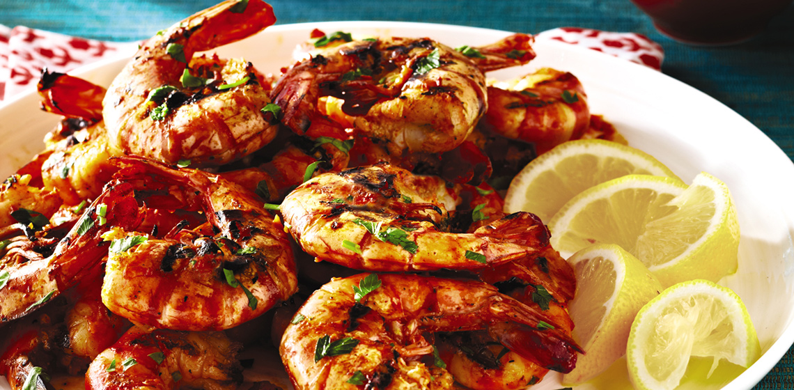 A white plate with a pile of grilled shrimp and slices of lemon.