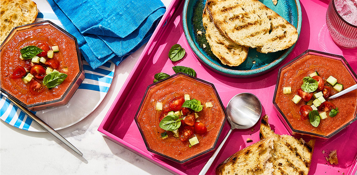 Bowls of summer gazpacho soup topped with cherry tomatoes, cucumber and fresh basil leaves. 