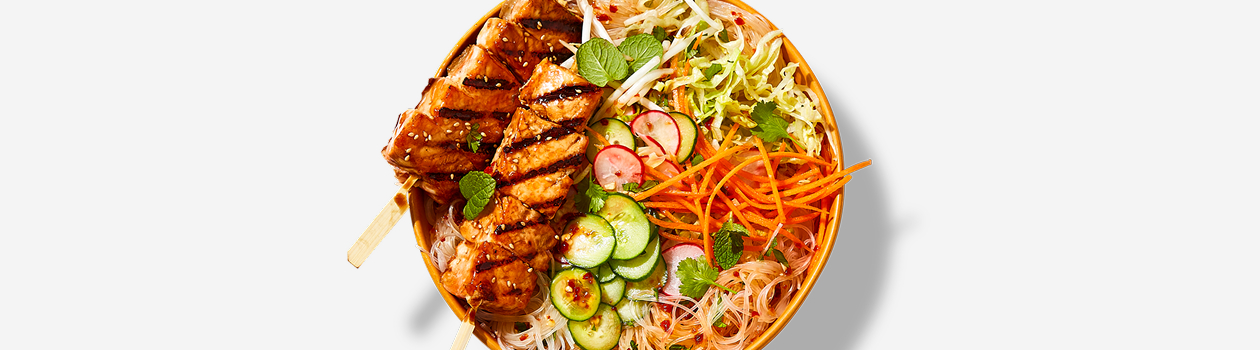 Bowl of rice noodle salad with two salmon skewers on top.