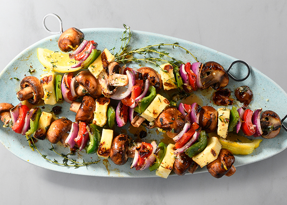 Four grilled cremini mushroom and halloumi cheese skewers on a blue plate.