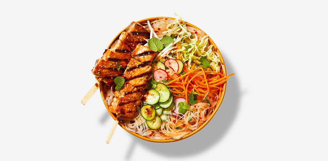 Bowl of rice noodle salad with two salmon skewers on top.