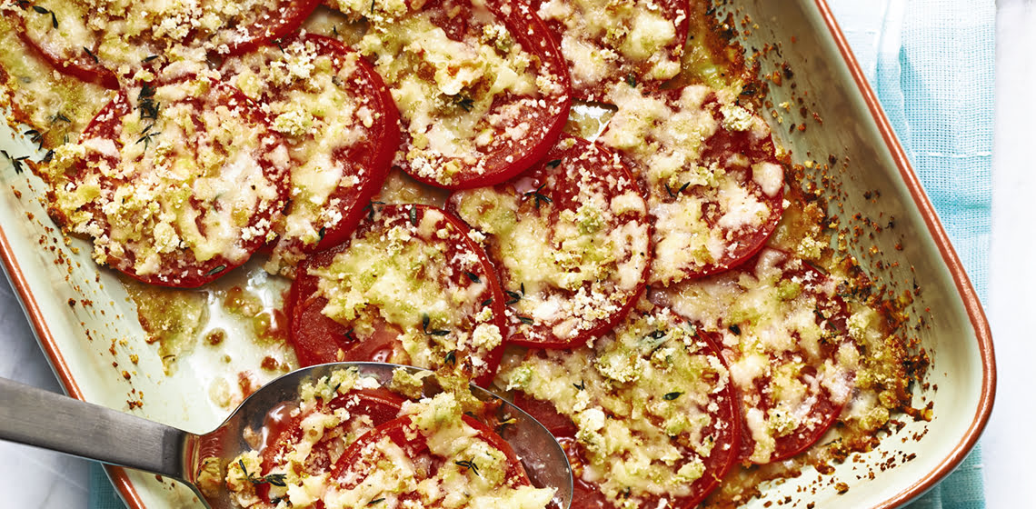 A large pan filled with the Tomatoes Provencal and a serving spoon with some on it.