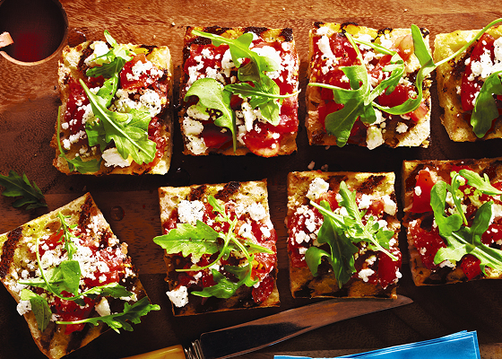 Pieces of bruschetta on a board topped with arugula.