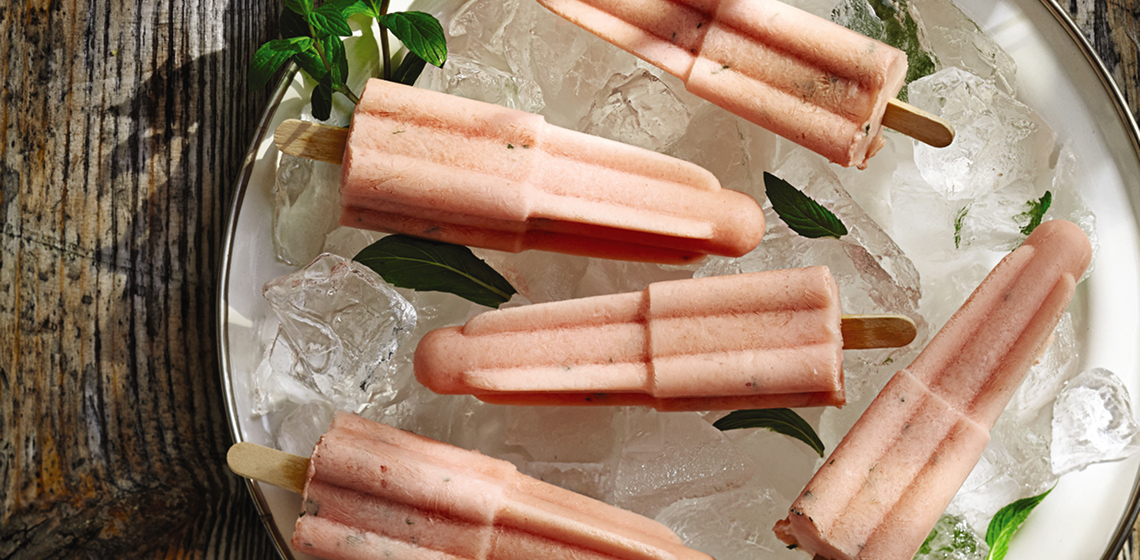 Overhead shot of five watermelon mint pops on ice on a white plate.