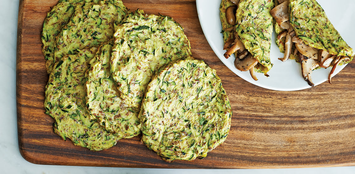 A bunch of flatbreads on a wooden board with a plate that features flatbreads as wraps with mushrooms inside.