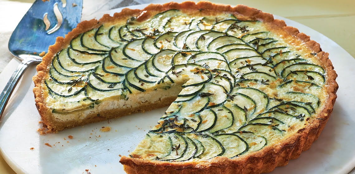 A zucchini tart on a white plate with a slice missing.