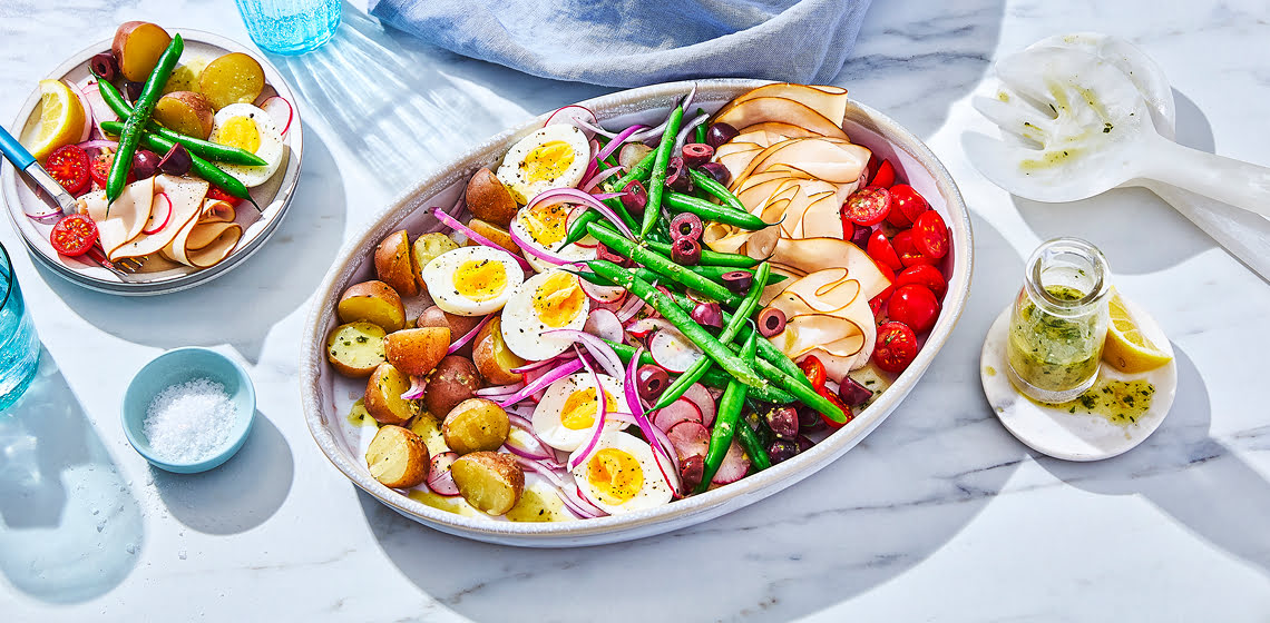 A platter of niçoise salad with beans, hard-boiled eggs, potatoes, radish, tomatoes, olives and cured meats.