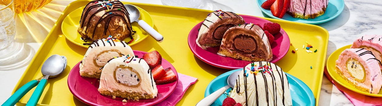 Six plates with the Dough Chi Ice Cream Bombes with some cut open to see the Dough Chi Bites and on the side there are berries and spoons.