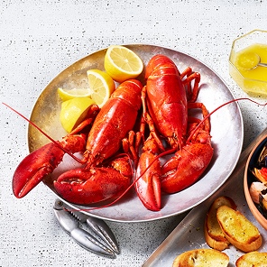 first-of-the-season__lobster Full cooked lobster in a bowl beside a plate of toasted bread.