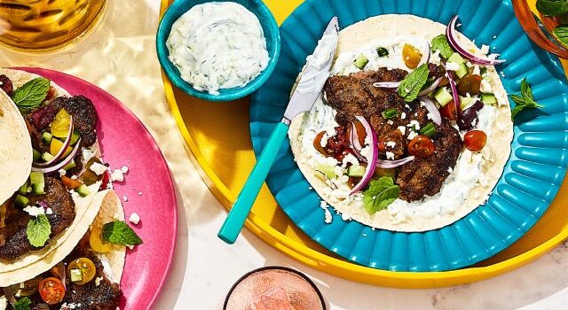Overhead shot of four Greek-inspired smashed burger tacos with tzatziki on the side.
