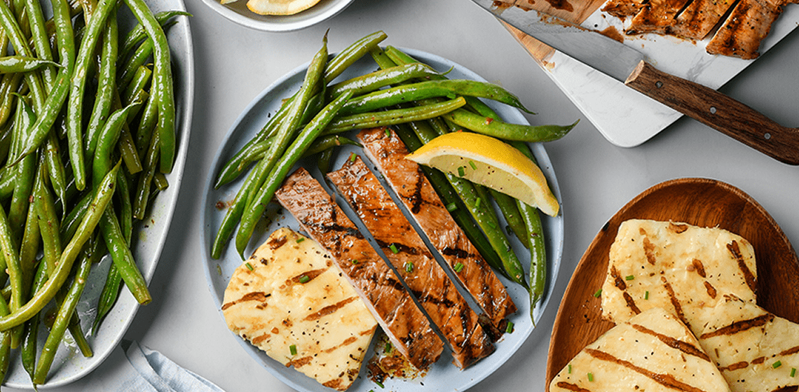Overhead shot of grilled pork tenderloin with side of green beans and halloumi cheese.