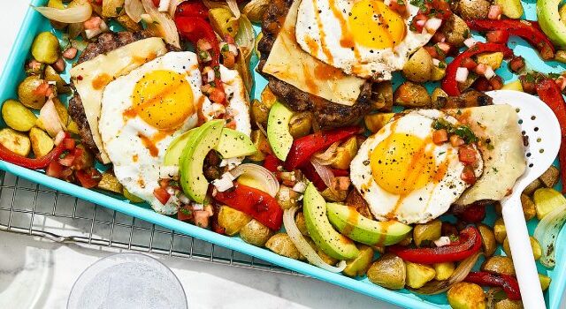 Mexican pan hash on a blue baking sheet with a bowl of tomato salsa and a plate of sliced avocado on the side.