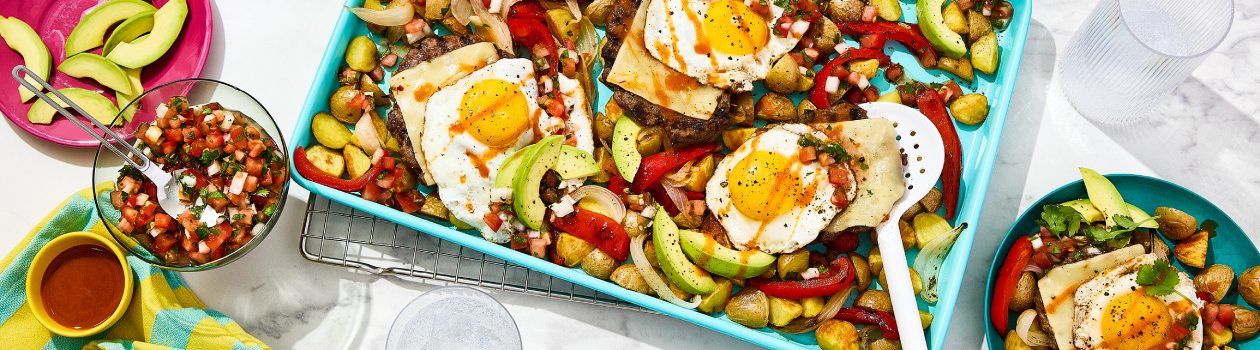Mexican pan hash on a blue baking sheet with a bowl of tomato salsa and a plate of sliced avocado on the side.