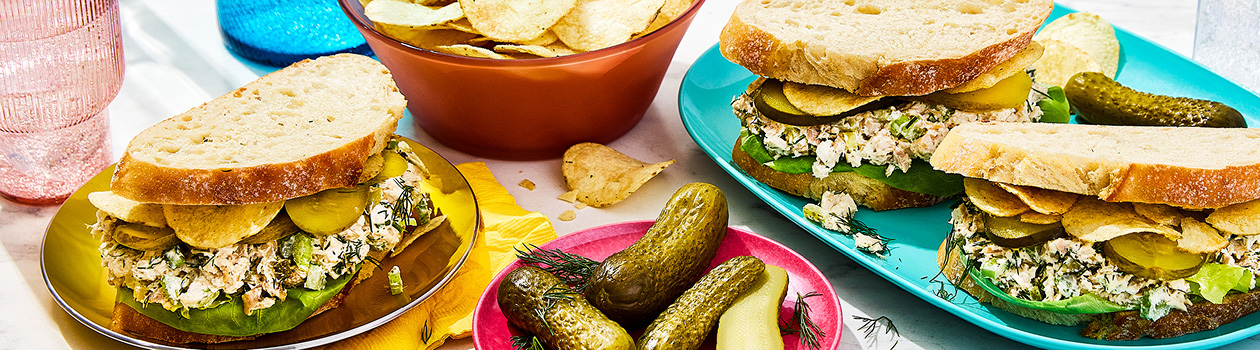 Three triple dill pickle chicken salad sandwiches, a plate of pickles and a bowl of chips.