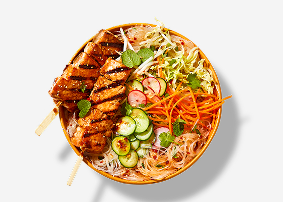Bowl of rice noodle salad with two salmon skewers on top.