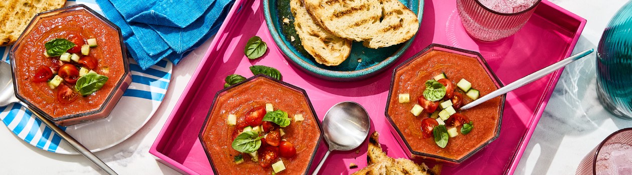 Bowls of summer gazpacho soup topped with cherry tomatoes, cucumber and fresh basil leaves.