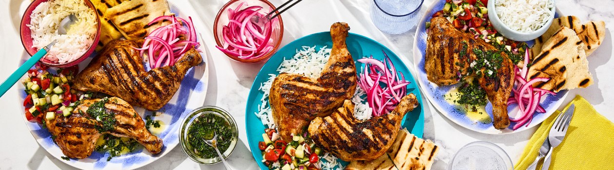 Three plates all with Tandoori Chicken, rice, kachumber salad, naan bread or pickled red onions with a small bowl of the pickled red onions and another with mint chutney.