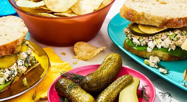Three triple dill pickle chicken salad sandwiches, a plate of pickles and a bowl of chips.
