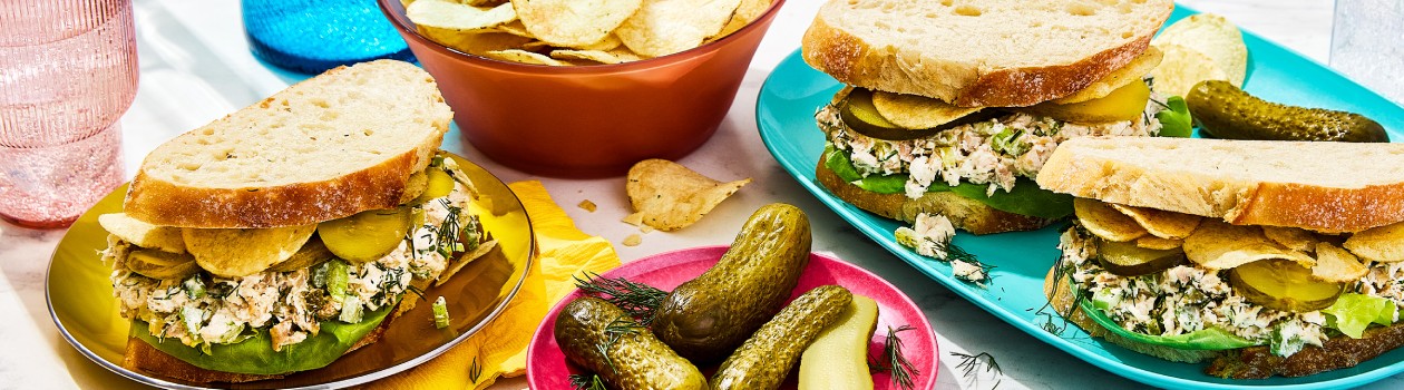 Three triple dill pickle chicken salad sandwiches, a plate of pickles and a bowl of chips.