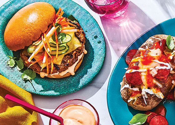Three different mash-up dishes with a burger, potatoes, and a corn dip, glasses of water, and a small bowl with a spread.