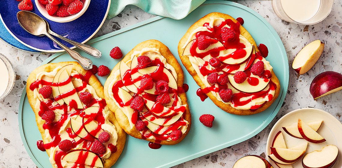 Overhead shot of three fried pastries topped with vanilla icing, raspberries, and sliced apples.