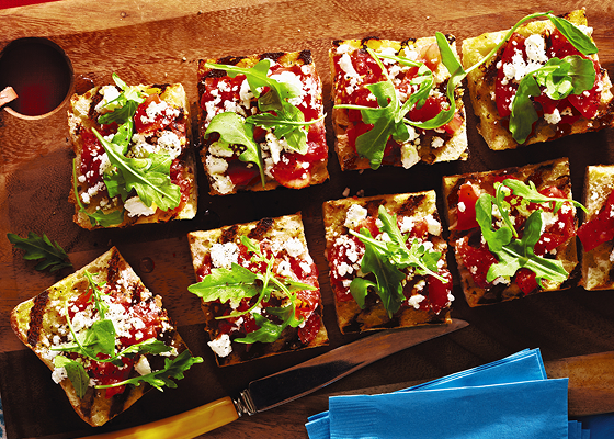 Pieces of bruschetta on a board topped with arugula