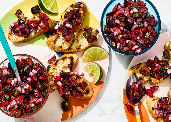 Two plates with crostinis topped with the cherry salsa and sliced limes, with bowls of the salsa and cherries on and around the plates.