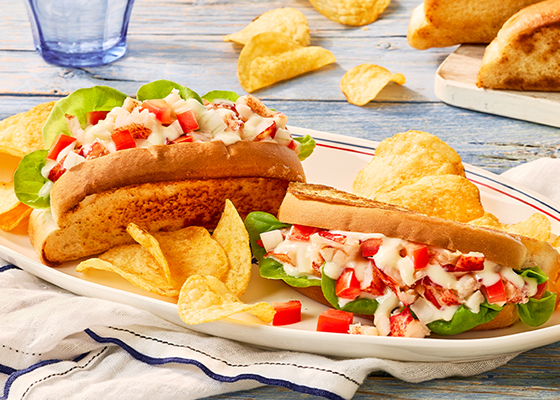 Two lobster rolls on a plate topped with Donair sauce with a side of chips