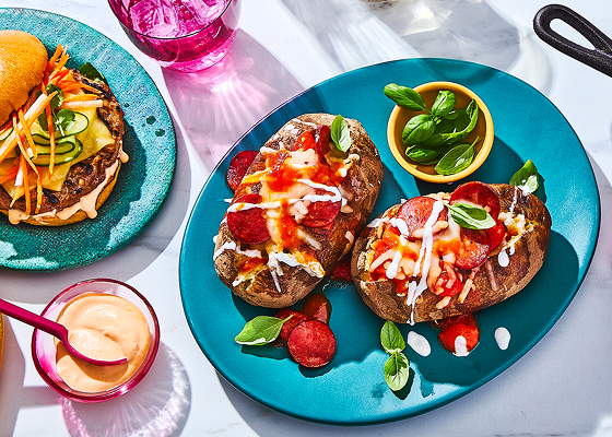 Three different mash-up dishes with a burger, potatoes, and a corn dip, glasses of water, and a small bowl with a spread.