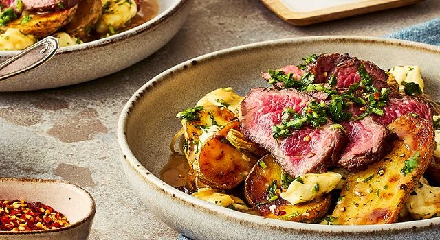 Two bowls of Argentinian poutine with two glasses of lemon water, a bowl of the chimichurri, and another small bowl with red pepper flakes.