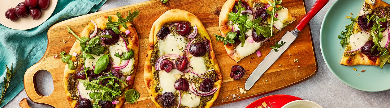 Two full cherry and basil flatbreads on a cutting board, and one that has been cut in half.