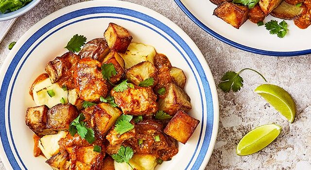 Three bowls of Butter Chicken Poutine with limes, cutlery, and herbs around the bowls on the table.