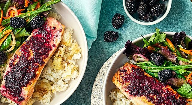Two crispy rice bowls topped with vegetables, salmon filet and a blackberry glaze.