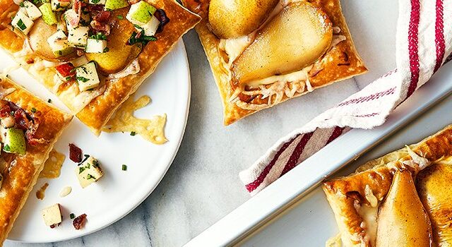 Three pear puff pastry tartlets on a plate, with two off to the side on a baking sheet.